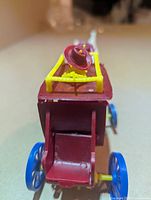 rear view of red stagecoach showing blue wheels and yellow roof rack with hats