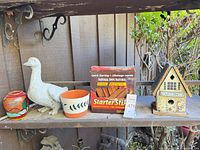 Shelf view with duck statue, pottery jar, ceramic planter, firestarter box and Garden Inn birdhouse