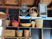Group of baskets on shelving including white metal wire stand, assorted brown wicker baskets, white wicker shelf