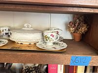 Shelf showing covered dish, cups, saucers, tray and dried flowers