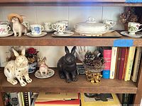 Overview of shelf with books, rabbit figurines, tea set, tureen and decor