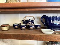 Shelf showing cobalt teapot, four cups, blue bowl, brass container, white dish