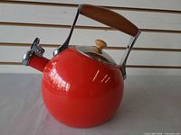 Side view of red Nambe whistling tea kettle showing wood handle and lid