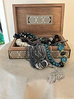 Open inlaid wooden jewellery box with visible assorted jewellery spilling out