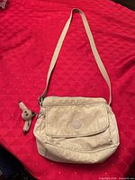 Full view of khaki Kipling bag with strap and keychain