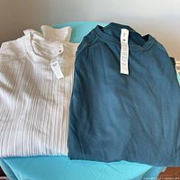 Blue It’s Rulu and white Rest Less tops folded showing textures and tags.