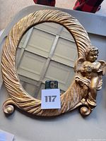 Front view showing oval gilded frame, cherub figure, mirror surface