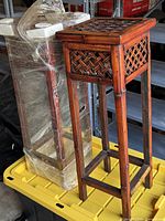 One unwrapped bamboo wood plant stand beside second stand wrapped in plastic film, showing lattice top and overall height