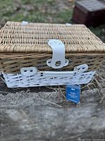 Front view of closed wicker picnic basket showing natural/white weave, white faux-leather latch, Pier 1 tag