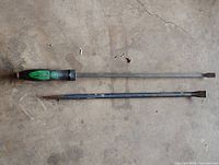 Two pry bars laid on concrete floor showing full length, ends and handle details