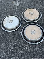 Three Cadillac hubcaps on pavement showing fronts and condition