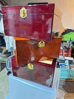 Stack of three glossy wood memorial chests showing front latches and varied finishes