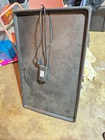 Full view of black rectangular heating mat with cord and thermostat