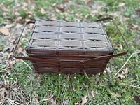 Closed brown wicker sewing basket with handles shown outdoors