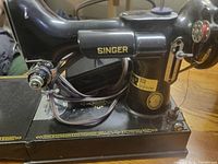 Left side view of Singer Featherweight sewing machine showing brand name and fold-down bed