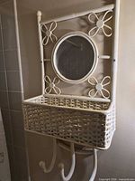 Front view of the white wicker wall shelf showing mirror, basket shelf, and hooks