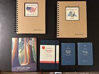 All five journals laid out: two kraft spiral, one illustrated softcover, one navy Moleskine, one pocket dark blue