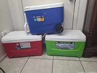 Three Igloo coolers stacked: blue wheeled 38 qt on top of red and green 48 qt chest coolers