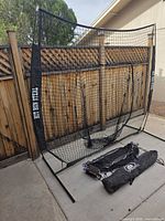 Full view of assembled Hit Run Steal batting net, two carry bags and glove on ground
