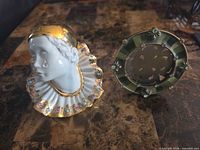Pierrot bust and round enamel frame side by side on tabletop