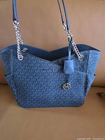 Front view of blue MK monogram tote showing overall design, handles, side pockets, logo charm