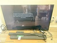 Front view of Panasonic TV, two soundbars, remotes and cables powered on showing message