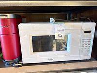 Front view of white Master Chef microwave beside red Keurig coffee maker, cords visible