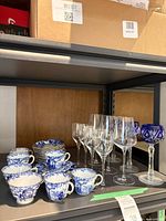 Shelf view showing cups, saucers, clear stemware, cobalt goblet