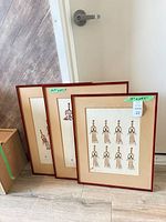 Three red-framed prints leaning against wall, showing sizes and styles