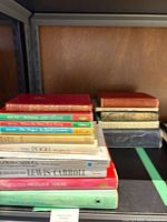 Stack of approximately twelve vintage hardcover books on shelf showing variety of colors and sizes