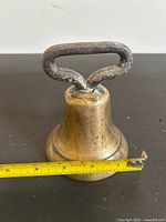 Side view of brass hand bell with measuring tape showing diameter