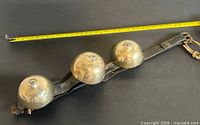 Full view of leather strap with three brass bells and measuring tape for length reference