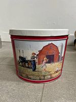 Front view of red tin with farm scene graphic and white lid