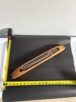 Full view of wooden boat shuttle beside tape measure showing length