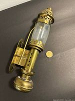 Full view of brass wall sconce with glass chimney and mounting plate, coin for scale