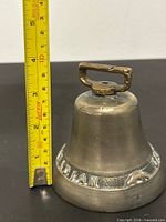 Front view of brass bell beside tape for scale showing height