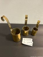 Three brass scoops standing upright showing size differences and capacity markings
