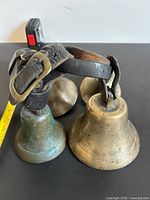 Group of four brass cowbells on leather straps, tape measure for scale
