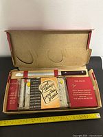 Open box showing slicing guide, knife, insert and red sleeves with measuring tape for scale