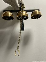 Front view of mounted triple brass bell set showing bells, bracket and chain