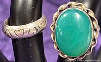 Close-up of two sterling silver rings displaying oval green chalcedony ring and heart-pattern band