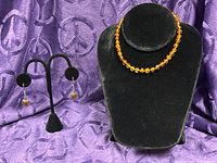 Necklace and earrings displayed on black velvet stands against purple fabric
