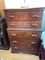 Front view of brown wood veneer five-drawer dresser showing all drawers, pulls, top molding and base