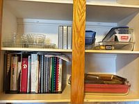 cabinet shelf with glass bakeware, plastic containers, cookbooks, red ceramic baker