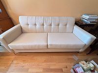 Full view of beige three-seat sofa with tufted back, straight arms, metal legs