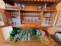 Overall cabinet view with clear crystal stemware on shelves and green/pink Depression-style glass on lower surface