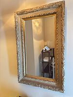 Full view of the ornate gold gilded wood framed wall mirror hanging vertically.