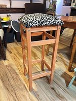 Full view of one wood bar stool showing light wood frame and leopard seat