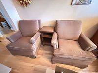 Front view of both beige fabric armchairs flanking wood side table