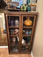 Front view of closed oak-tone curio cabinet with glass doors and items displayed on top